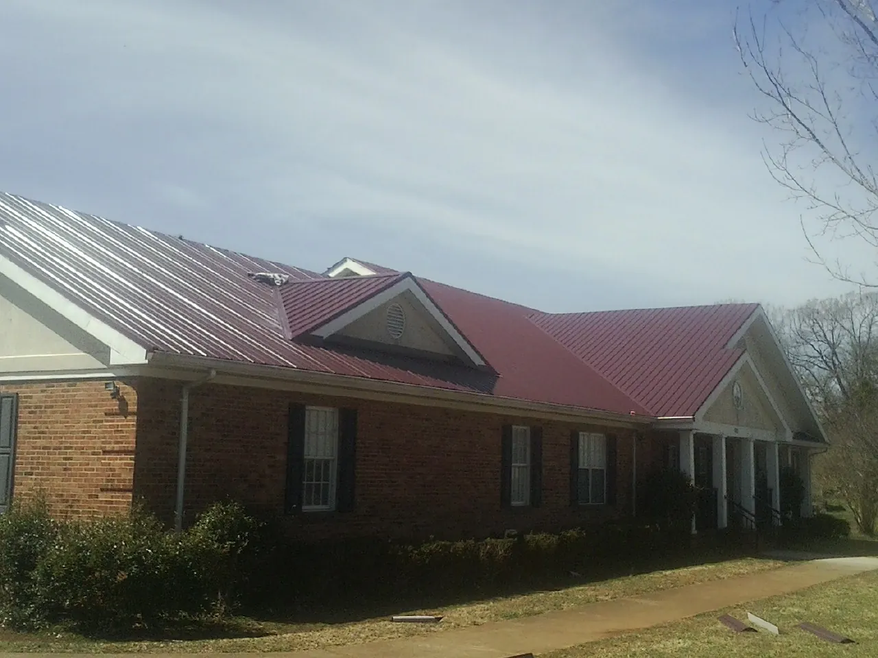 Red metal roof with gabled entries on a long brick building, from a Hail Damage Roof Repair job in Shavertown
