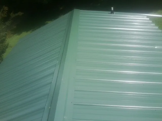 New green metal panels meeting at the ridge of a roof — Flat Roof Repair work by our crew in Shavertown
