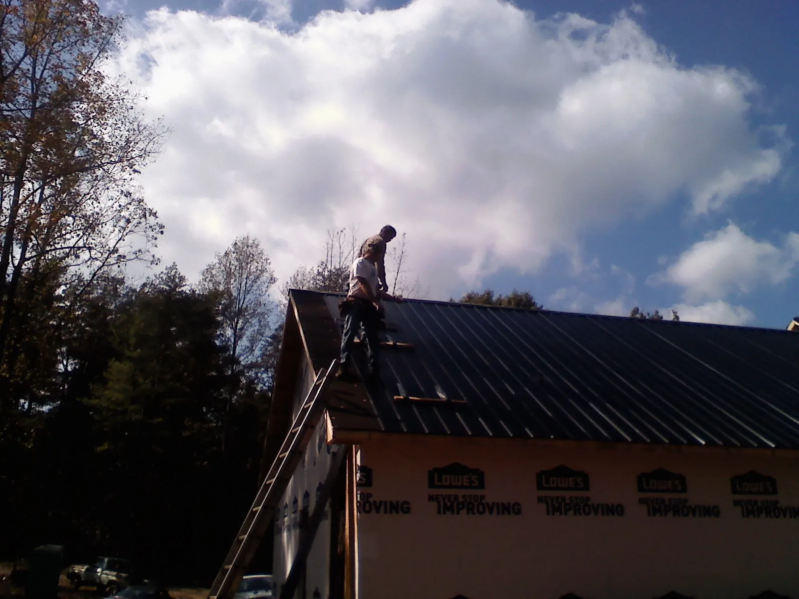 Roofer fastening dark metal panels high against a cloudy sky, from a Roof Inspection job in Shavertown