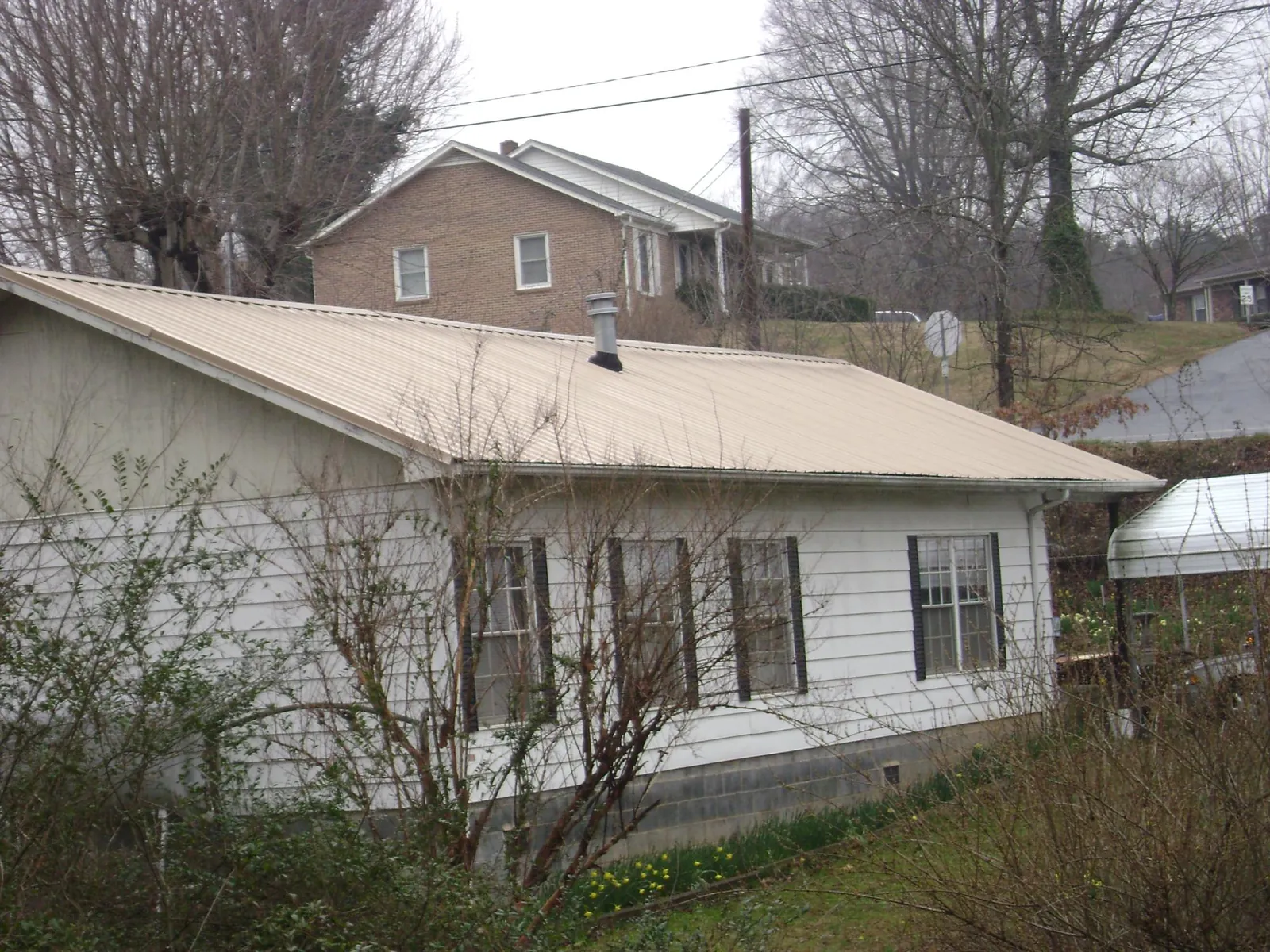 Tan metal roof on a white sided house set into a hillside — Commercial Roofing by Roofing Brothers in Shavertown